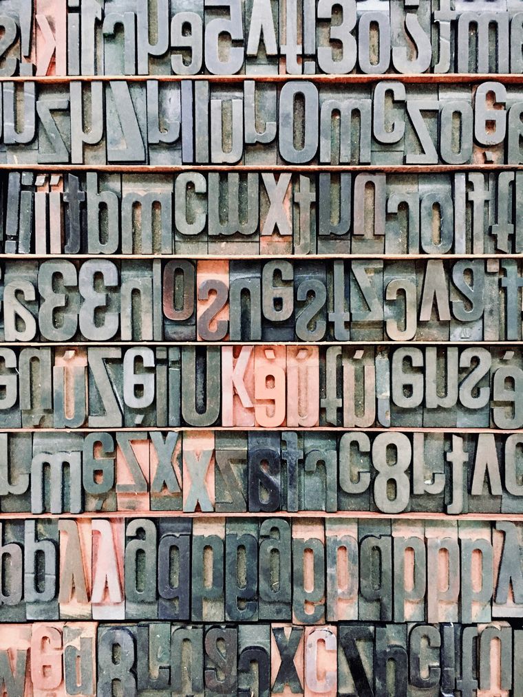 Close-up of vintage metal letterpress type blocks arranged in rows, showing reversed letters and numbers in various fonts and sizes.